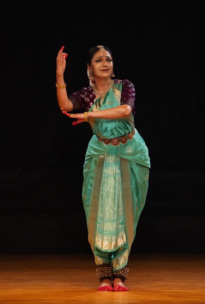 Rama Vaidyanathan performing Bharatanatyam in a turquoise costume against a dark stage